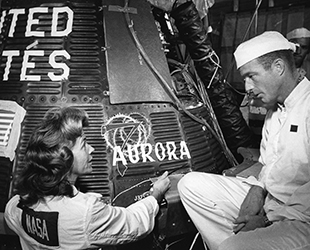 Cece Bibby and Scott Carpenter inspect her hand-painted Aurora insignia on the Mercury-Atlas 7 capsule
